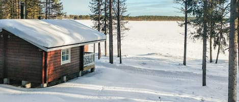 A wooden cabin with a snow-covered roof, surrounded by trees and a snowy landscape.