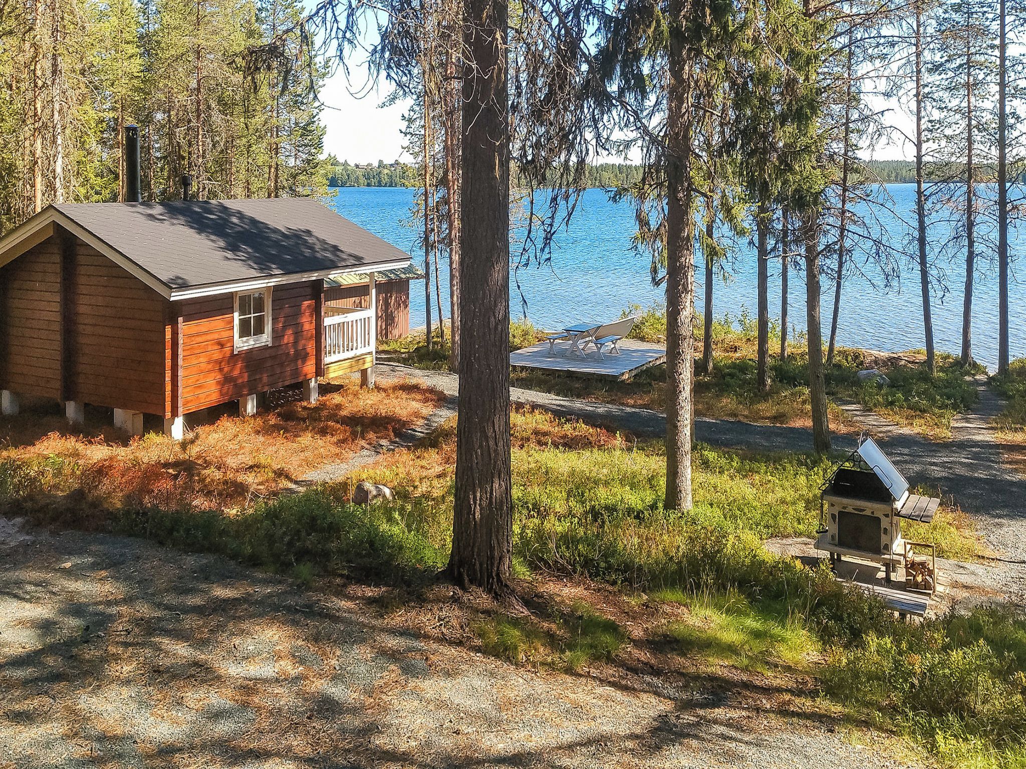 A cabin with a deck overlooking a lake, surrounded by trees.