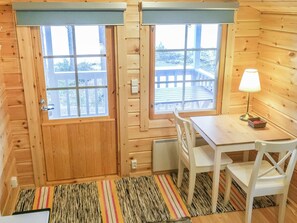 L’intérieur d’un chalet en bois comprend un coin repas, deux fenêtres, une table, des chaises, une lampe et un tapis.