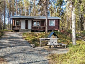 A cabin with a porch, a chimney, and a birdhouse in a forest setting.
