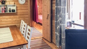 Een houten interieur met een eettafel, stoelen, een gestreept vloerkleed, een boekenkast en een gordijn met een patroon.