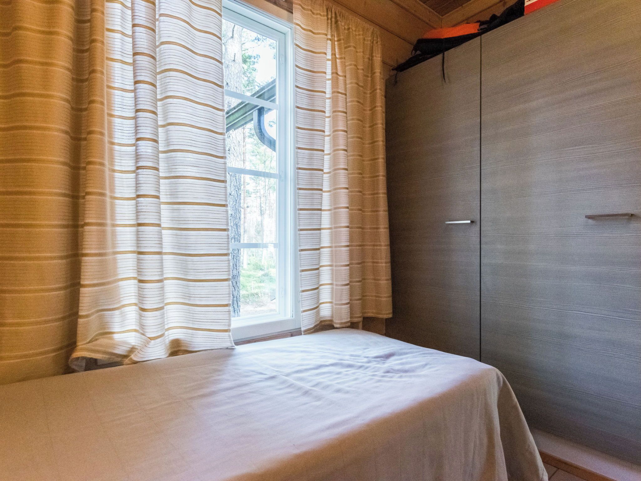 Una habitación con cama, ventana con cortinas y armario.