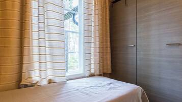 Una habitación con cama, ventana con cortinas y armario.