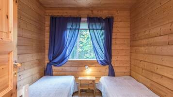 Eine kleine Holzhütte mit zwei Betten, einem Fenster mit Vorhängen, einem Nachttisch und einer Lampe.