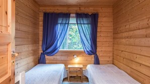 A small wooden cabin room with two beds, a window with curtains, and a nightstand. - Aamuntorkku by Interhome (Punkaharju)