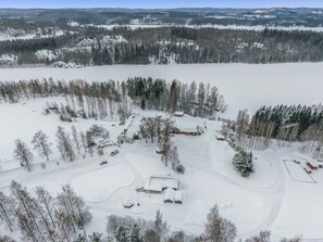 Lumipeitteinen maisema, jossa on useita rakennuksia, mukaan lukien päärakennus, jossa on suuri kuisti, sekä sen lähellä sijaitseva pienempi rakennus.