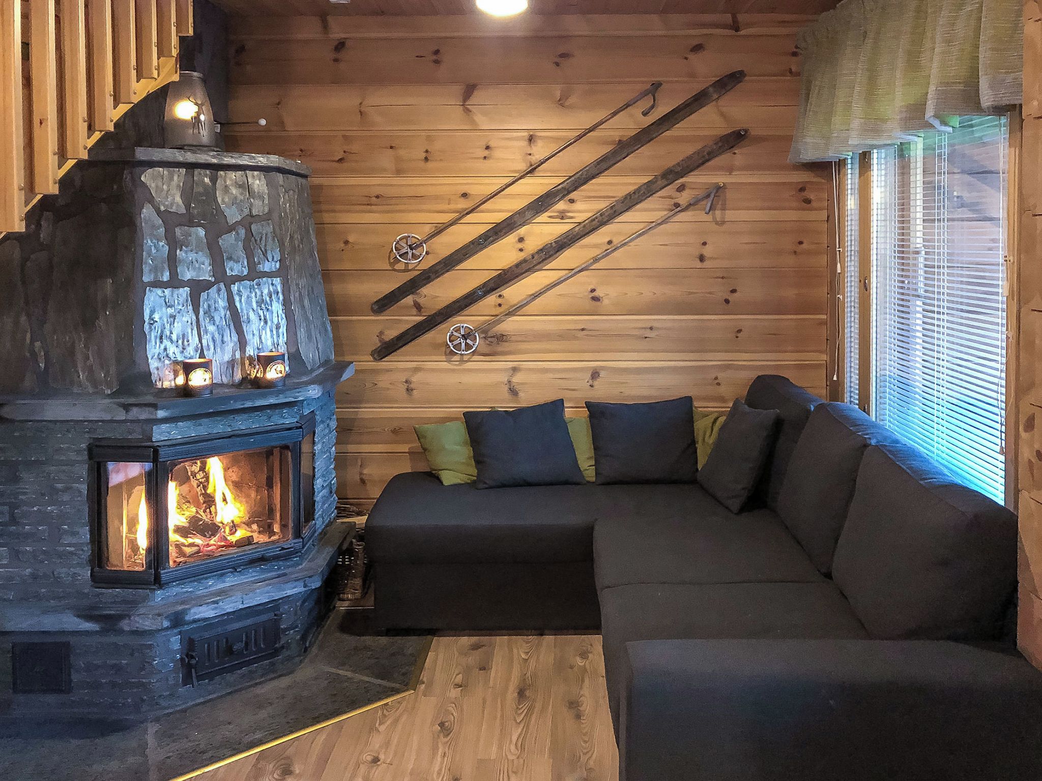 A cozy cabin interior with a stone fireplace, a wooden ceiling, and a sofa with cushions.