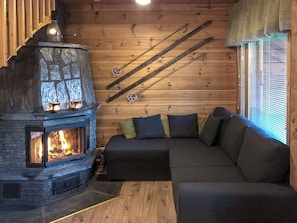 Un interior de cabaña acogedor con chimenea de piedra, techo de madera y un sofá con cojines.