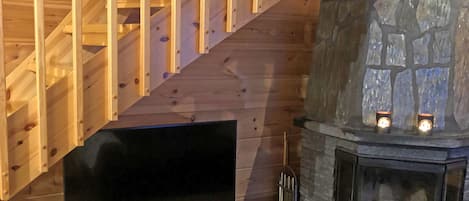 A wooden staircase, a stone fireplace with two lit candles, and a television on a stand.