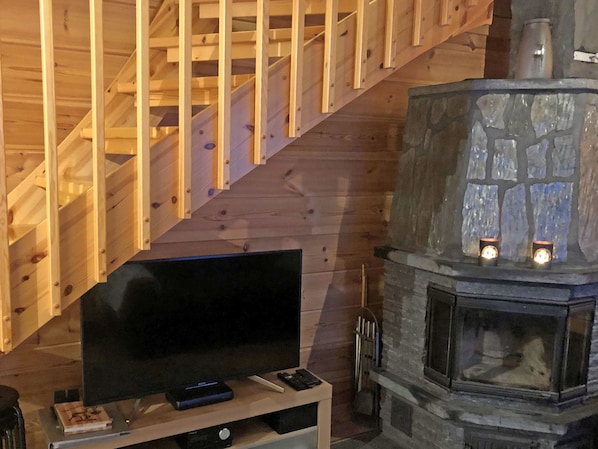 A wooden staircase, a stone fireplace with two lit candles, and a television on a stand.
