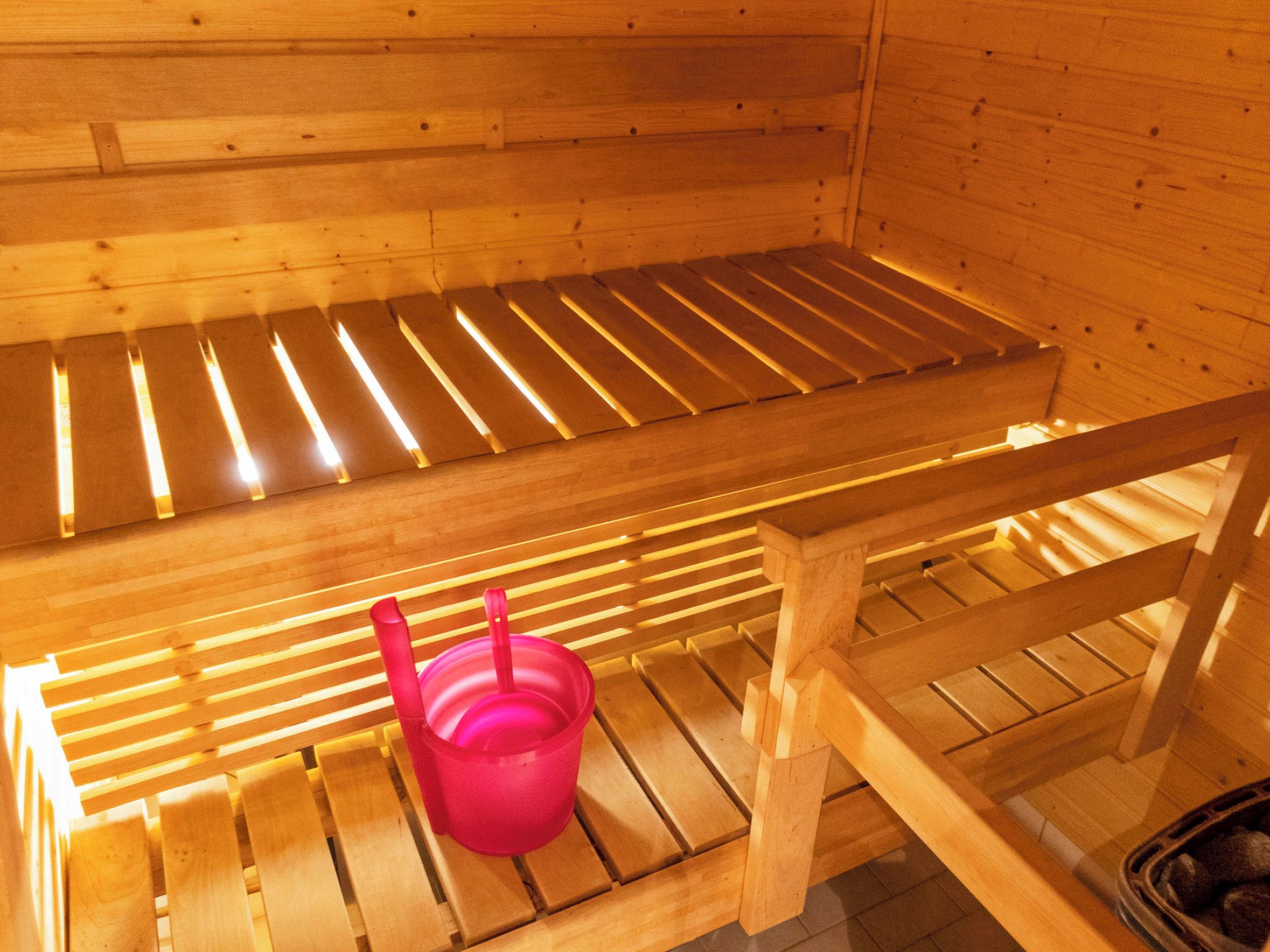 Uma sauna de madeira com bancos e um balde rosa.