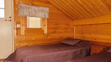 A cabin with two beds, a window with blinds, and a wooden ceiling.