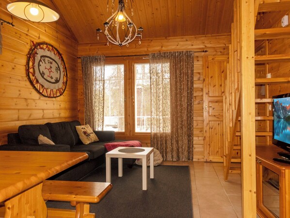 A cozy cabin interior with a wooden interior, a sofa, a small table, a television, and a chandelier.
