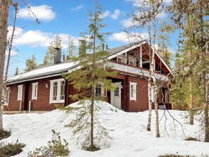 Una cabaña de madera con balcón, rodeada de nieve y árboles.