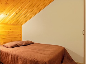 A single bed with a brown quilt in a room with wooden ceiling beams and white walls. - Hirvas levi 3 by Interhome (Kittilä)