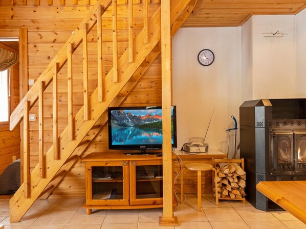 A wooden interior with a staircase, a television, a radio, and a fireplace.