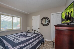 Un dormitorio con cama, cómoda, televisor y ventana con persianas.
