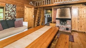 A cozy cabin interior with a wooden dining table, a sofa with cushions, a brick fireplace, and a ladder leading to an upper level.