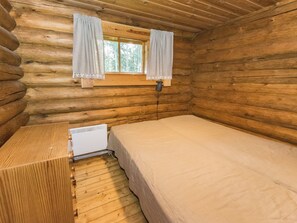 Una habitación tipo cabaña de madera con una cama individual, una mesita y una ventana con cortinas.