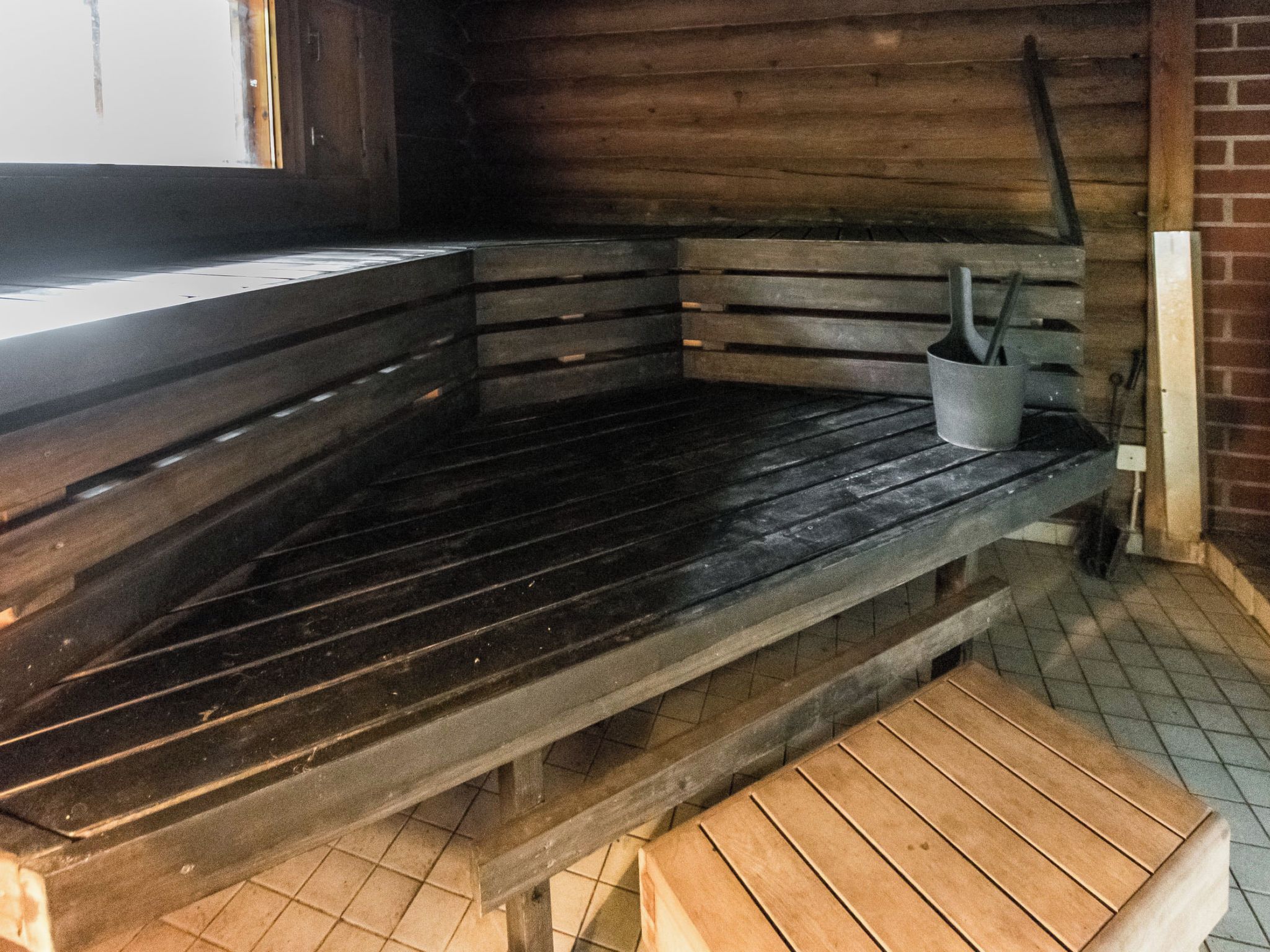 A wooden bench with a metal bucket, a wooden table, and a tiled floor.