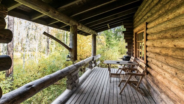 A wooden cabin with a deck, a table, and chairs.