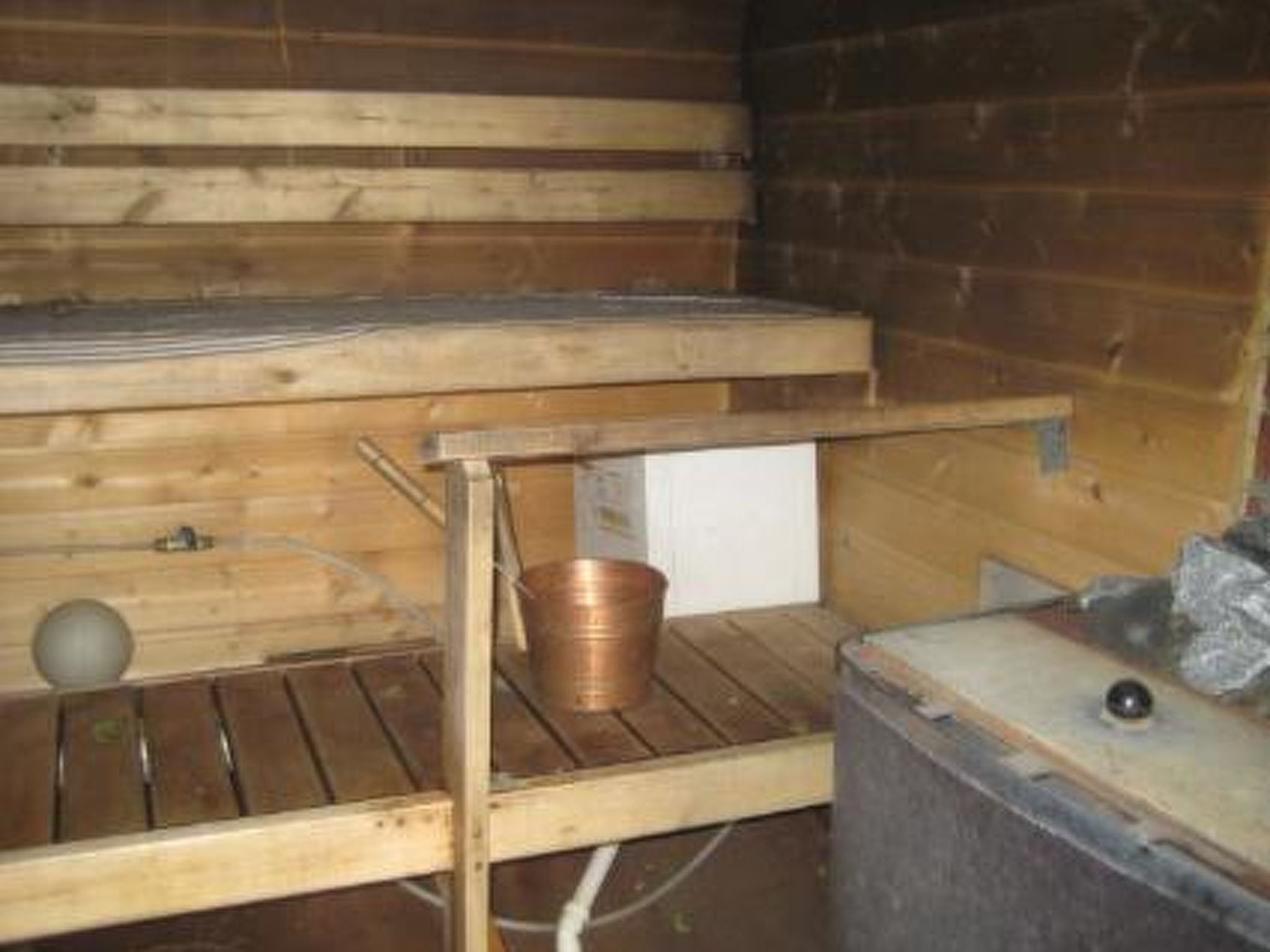 Interior de una cabaña de madera con literas, una mesita y un balde de metal.
