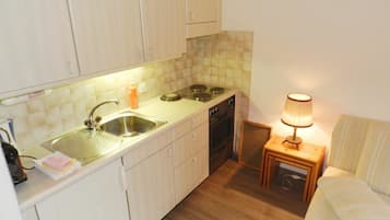 Een koelkast, een oven, kookgerei, borden en bestek, een eettafel