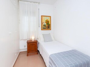 A bedroom with a bed, a nightstand, a painting, and a window with curtains.