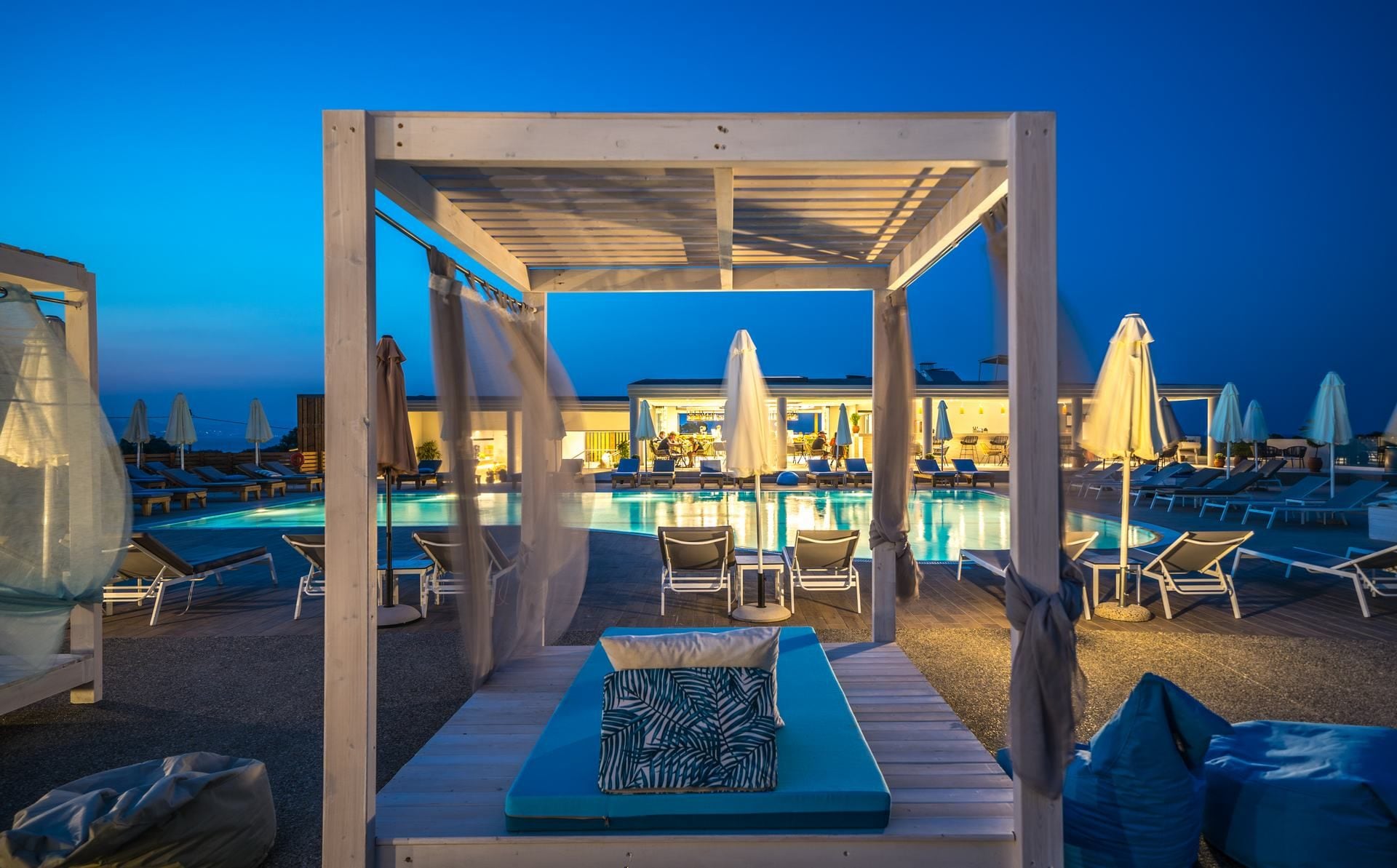 A poolside area with lounge chairs, umbrellas, and a covered seating area with cushions.