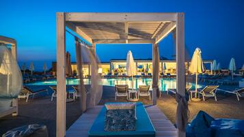 A poolside area with lounge chairs, umbrellas, and a covered seating area with cushions.