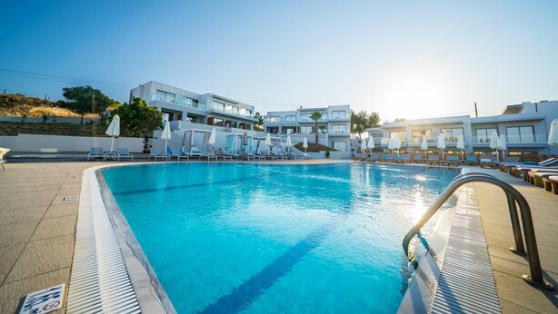A swimming pool with lounge chairs and umbrellas, surrounded by modern buildings. - Harmony Crest Resort& SPA (Kos)
