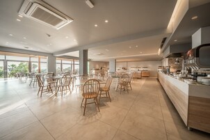 A spacious dining area with high ceilings, large windows, and a modern kitchen visible in the background.