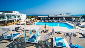 Uma área à beira da piscina com espreguiçadeiras, guarda-sóis e vista desimpedida para o mar.