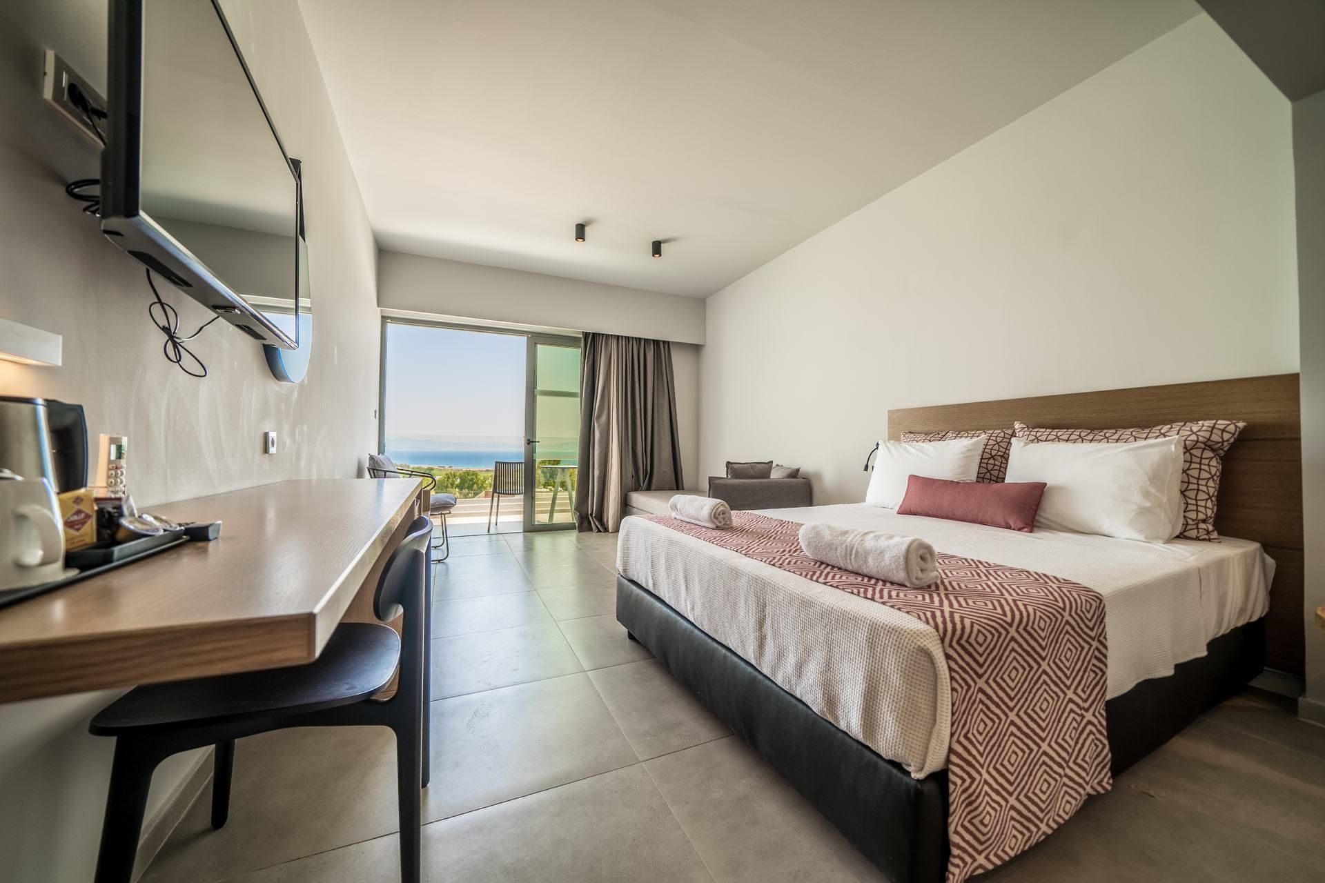 A modern hotel room with a large bed, a desk, and a view of the ocean.