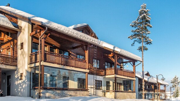 A multi-story wooden building with balconies, large windows, and a stone foundation.