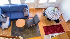 A modern living room with a blue sofa, a round wooden table, and a dining table with chairs.