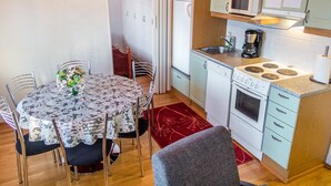 A compact kitchen with a microwave, stove, and dishwasher. A dining table with chairs is in the foreground.