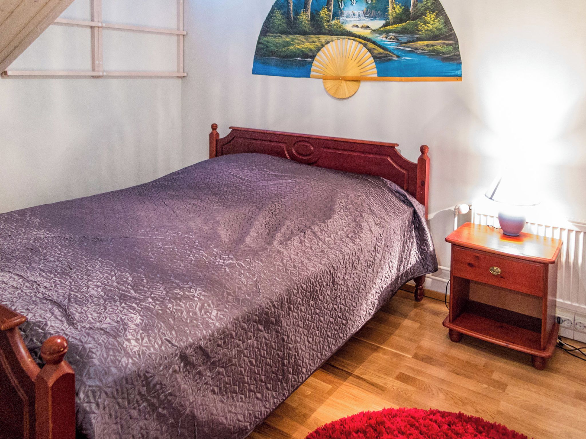 A bedroom with a bed, a nightstand, a lamp, and a painting on the wall.
