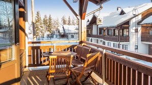 A wooden deck with a table and chairs, overlooking a snowy mountain landscape.