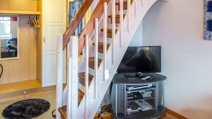 A modern living room with a wooden staircase, a flat-screen TV, and a media console.