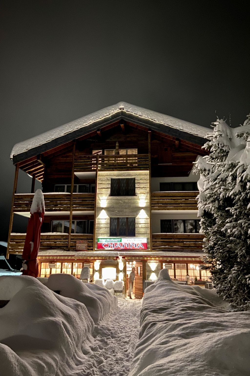 A wooden building with a sign reading "CHANNA" at the entrance, surrounded by snow.