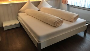 A neatly made bed with white linens and pillows, a bedside table, and a wall-mounted light fixture. - Apartment Channa by Interhome (Saas-Almagell)
