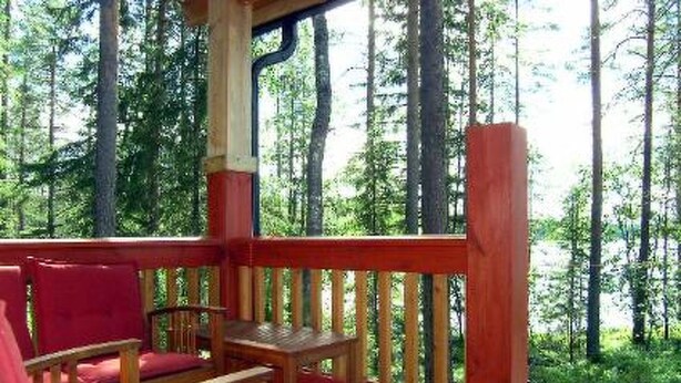 Una terraza de madera con barandas rojas y asientos, rodeada por un área boscosa.