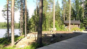 Una terraza de madera que lleva a una cabaña junto a un lago, rodeada de altos árboles.