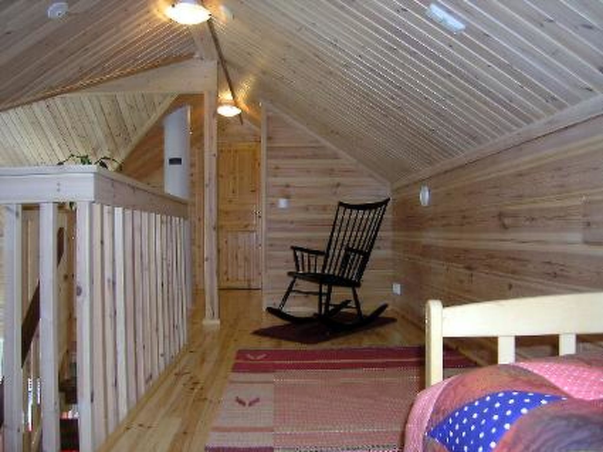 Un dormitorio estilo altillo acogedor, con techo de madera, una mecedora, una cama con colcha y una pequeña mesa con silla.
