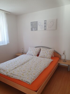 Un dormitorio con cama, dos mesitas de noche, una ventana con cortinas y decoración en la pared.