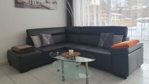 A modern living room with a dark grey sofa, two decorative pillows, a glass coffee table, and a 'HOME' sign on the wall. - Haus Artemis by Interhome (Saas-Grund)