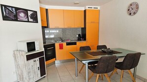 A compact kitchen with orange cabinets, a microwave, and a dining area with four chairs. - Haus Artemis by Interhome (Saas-Grund)