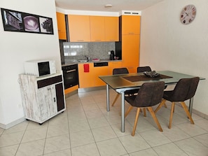 Una cocina compacta con armarios naranjas, un microondas y un comedor con cuatro sillas.
