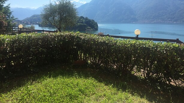 A view from a covered terrace overlooking a lake with mountains in the background.